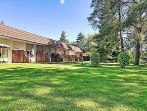 A row of single-story buildings with a tiled roof, a grassy lawn, and trees in the background. - Nice apartment in villa for 6 guests with WIFI, TV, terrace and pets allowed (Waren)