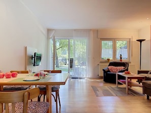 Una sala de estar moderna con comedor, un sofá, una mesa de centro y un televisor montado en la pared.