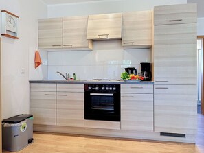 Eine moderne Küche mit hellen Holzschränken, einem eingebauten Backofen und einer Kaffeemaschine auf der Arbeitsfläche.