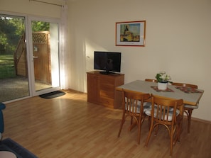Una habitación con una mesa de comedor de madera, sillas, un televisor sobre un mueble de madera y un ventanal corredizo que da a un espacio al aire libre.