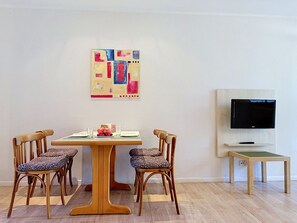 Ein Essbereich mit einem Holztisch und Stühlen, einem Bild an der Wand und einem Fernseher auf einem Schrank.
