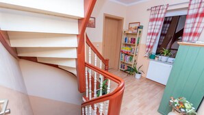 A spiral staircase with wooden steps and white balusters, leading to a landing with a bookshelf and a radiator. - Beautiful apartment for 4 guests with WIFI, TV and patio (Hettstedt)