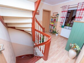 A spiral staircase with wooden steps and white balusters, leading to a landing with a bookshelf and a radiator.