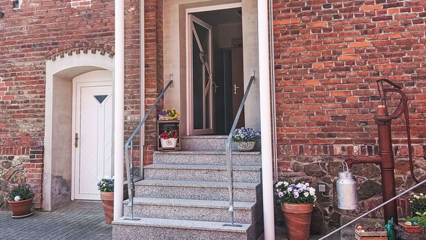 A brick building with a white door, a set of stone steps leading to an entrance, and potted plants. - Beautiful apartment for 4 guests with WIFI, TV and patio (Hettstedt)