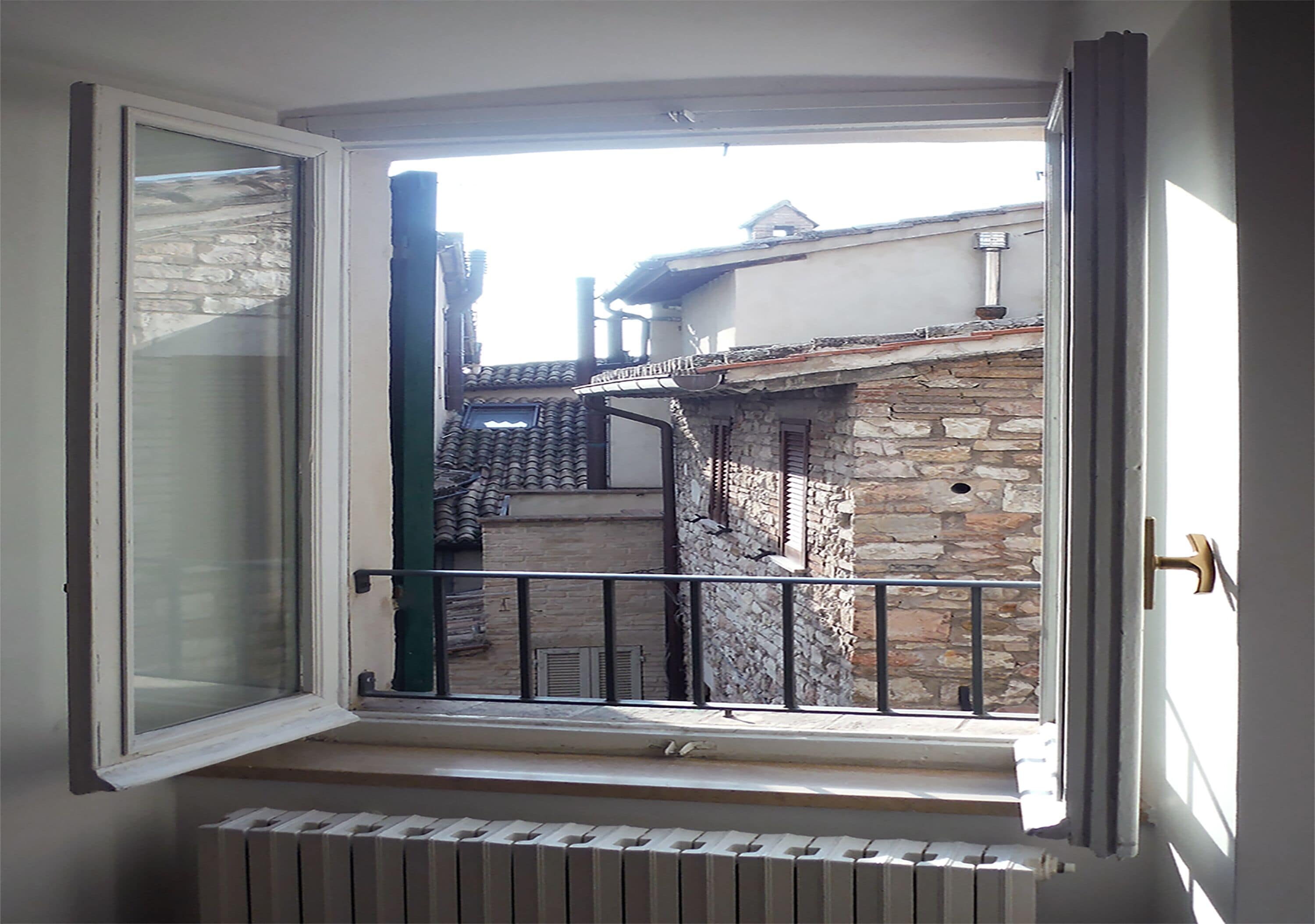 A room with a large window overlooking a courtyard with stone buildings and a metal railing.
