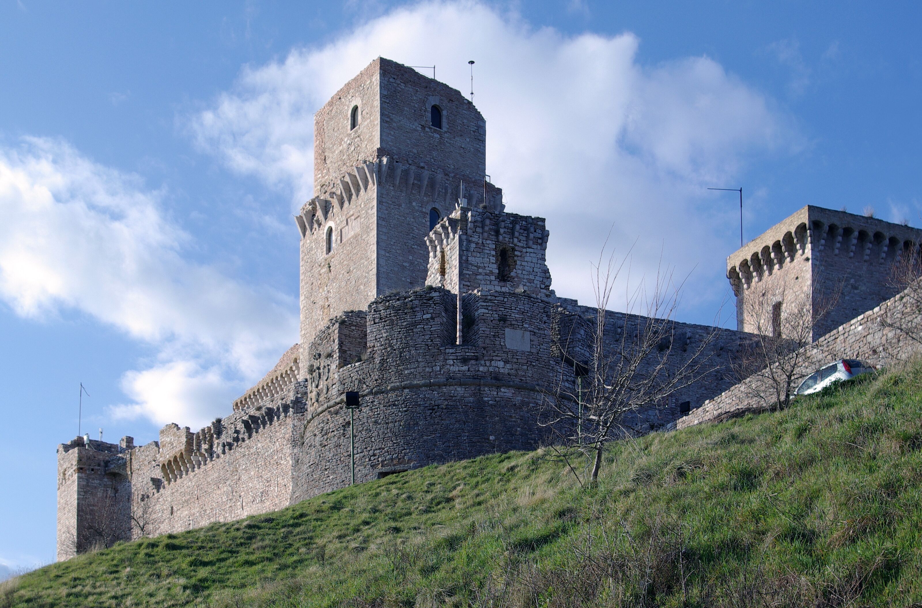 A historic stone castle with a prominent tower and battlements, situated on a grassy hill.