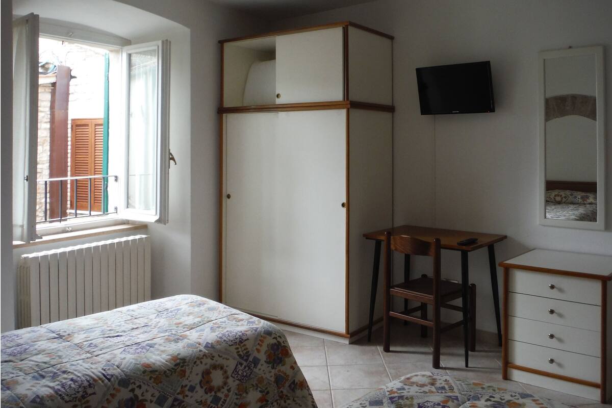A bedroom with a bed, a wardrobe, a desk, a chair, a television, and a radiator.