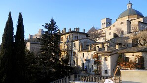 A courtyard with stone buildings, a white chair, and a staircase. - Camere Gambacorta (Assisi)
