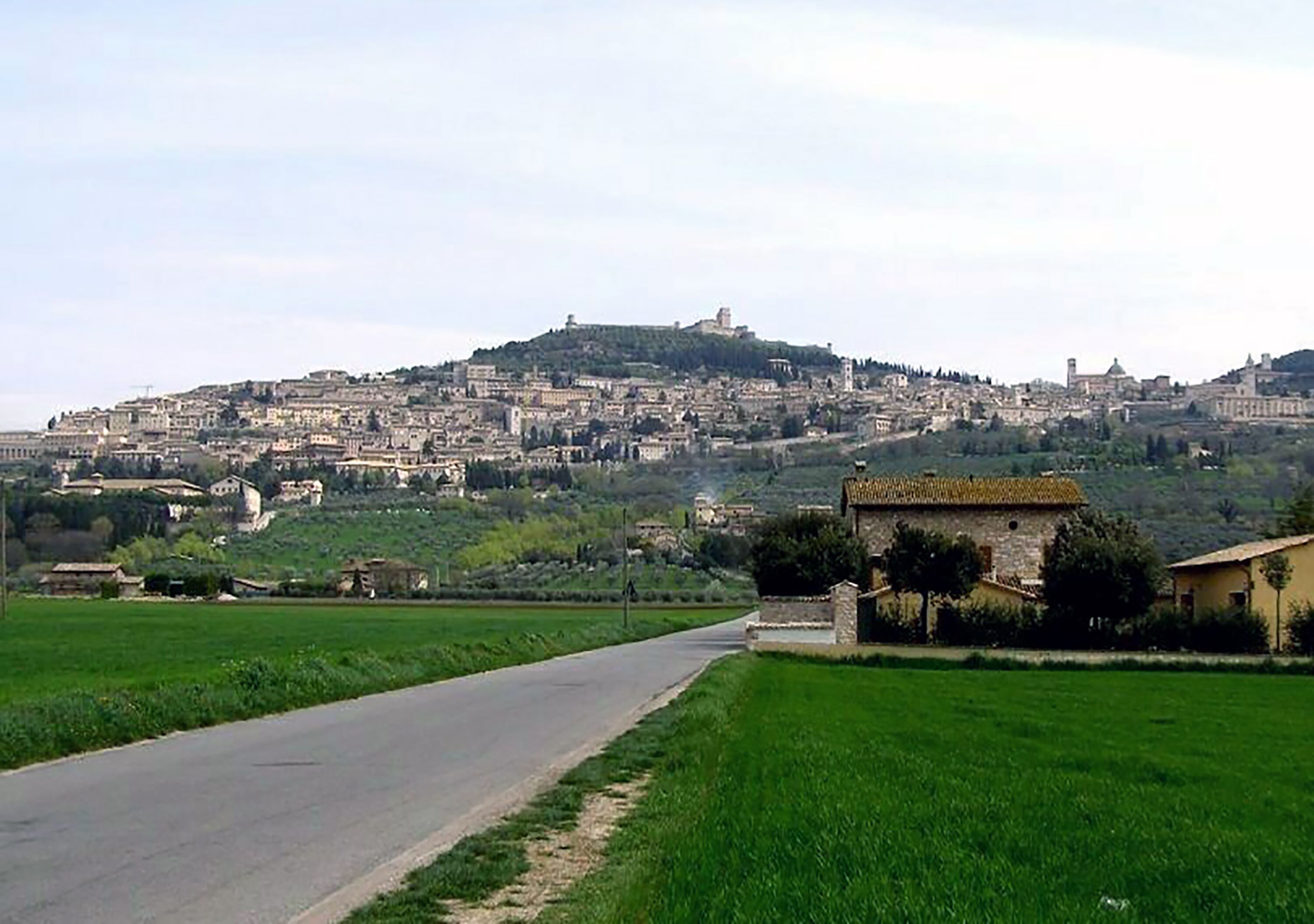 A road leading to a hilltop town with historic buildings and a prominent tower.