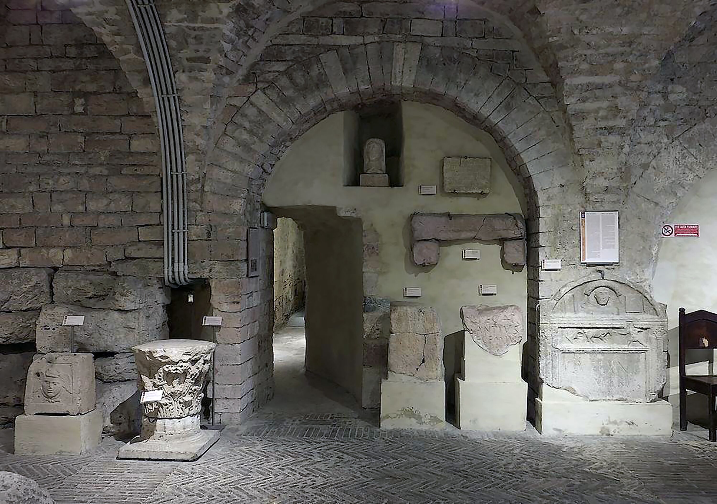 An arched stone corridor with ancient wall decorations and a tiled floor.