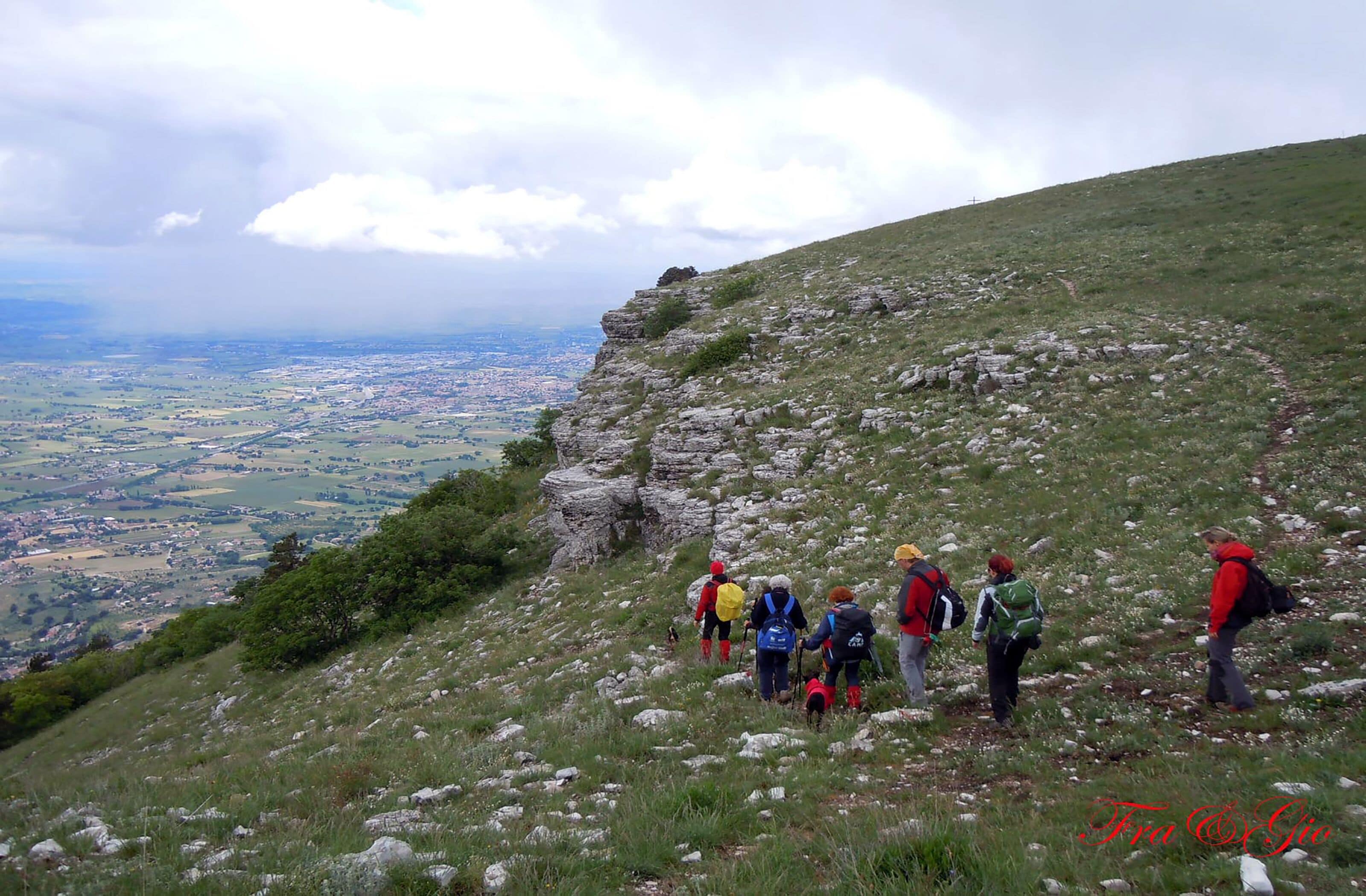 A group of hikers on a grassy hill with a view of a valley below.