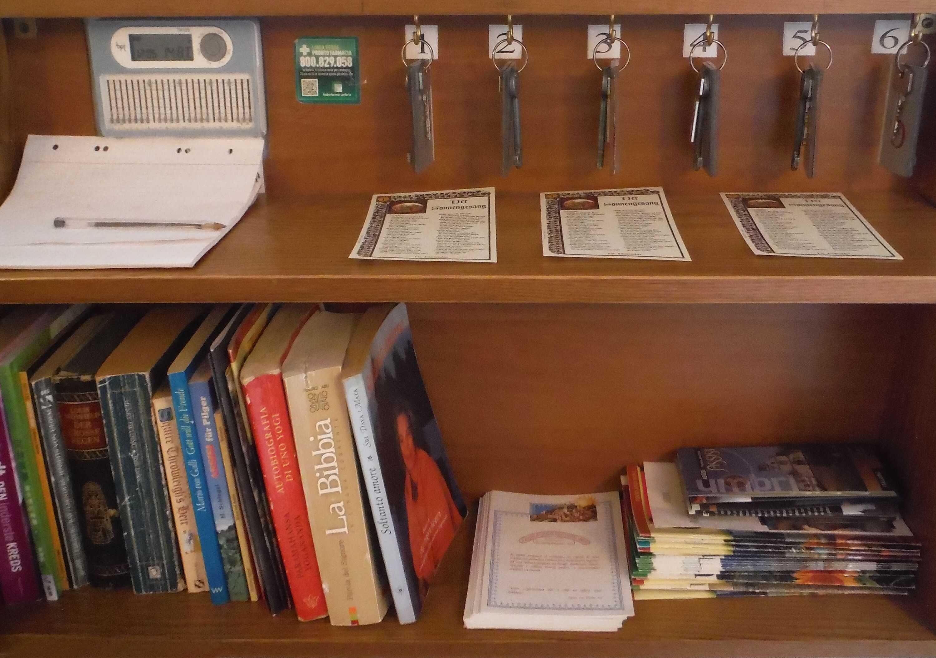 Una scrivania di legno con chiavi appese a un portachiavi, un quaderno e documenti. In basso, si vedono libri e riviste.