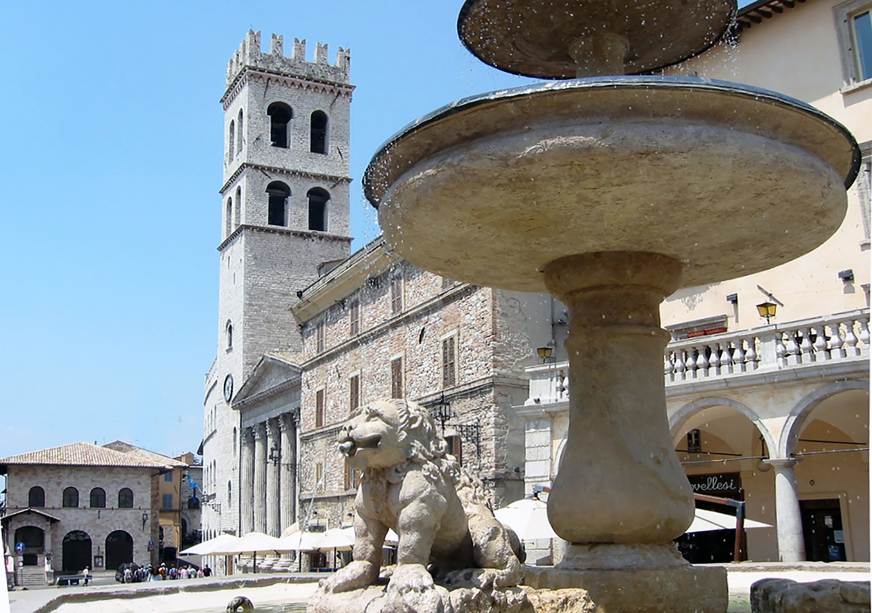 A historic fountain with a lion statue in a square with a church tower in the background.