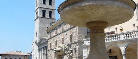 A historic fountain with a lion statue in a square with a church tower in the background.