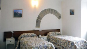 A hotel room with two beds, a nightstand, a wall-mounted lamp, and a decorative stone arch. - Camere Gambacorta (Assisi)