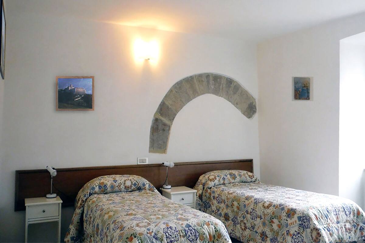 A hotel room with two beds, a nightstand, a wall-mounted lamp, and a decorative stone arch.