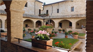A courtyard with stone buildings, arched walkways, and potted plants. - Camere Gambacorta (Assisi)