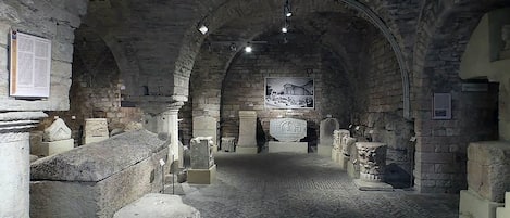 An underground passage with stone walls and arches, featuring ancient stone artifacts and inscriptions.