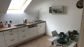 A modern kitchen with a skylight, white cabinets, a dishwasher, and a dining area with a table set for two. - New holiday apartment / fitter apartment Matthies (Kürten)