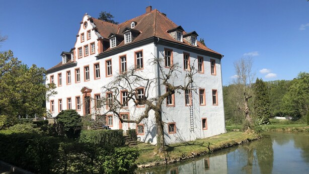 A large, historic building with multiple windows and a red-tiled roof, surrounded by a pond and greenery. - New holiday apartment / fitter apartment Matthies (Kürten)