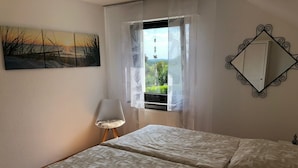 A bedroom with a bed, a chair, a window with curtains, a painting, and a mirror on the wall. - New holiday apartment / fitter apartment Matthies (Kürten)
