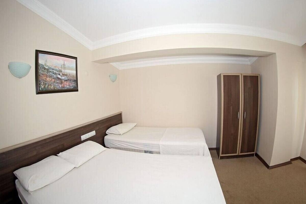 A hotel room with two single beds, a wooden wardrobe, a framed painting, and a decorative wall light.