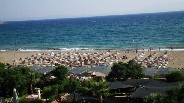 A beach with rows of umbrellas and beach chairs, a clear sky, and the ocean. - Adahan Hotel (Menderes)