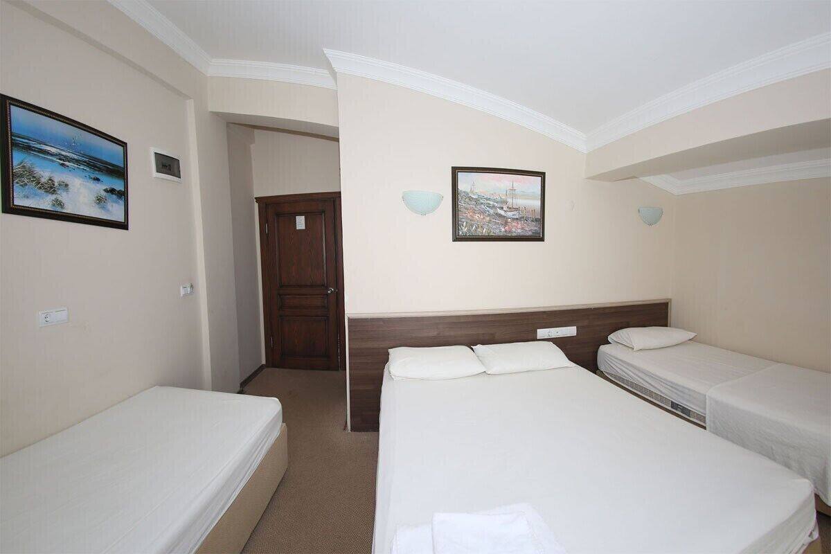 A hotel room with two single beds, a wooden headboard, a painting of a coastal scene, and a door leading to another room.