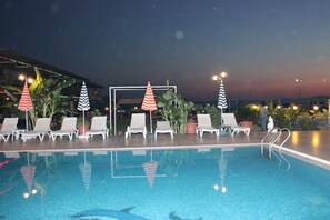 An indoor swimming pool with lounge chairs and umbrellas, surrounded by potted plants and a night sky view. - Adahan Hotel (Menderes)