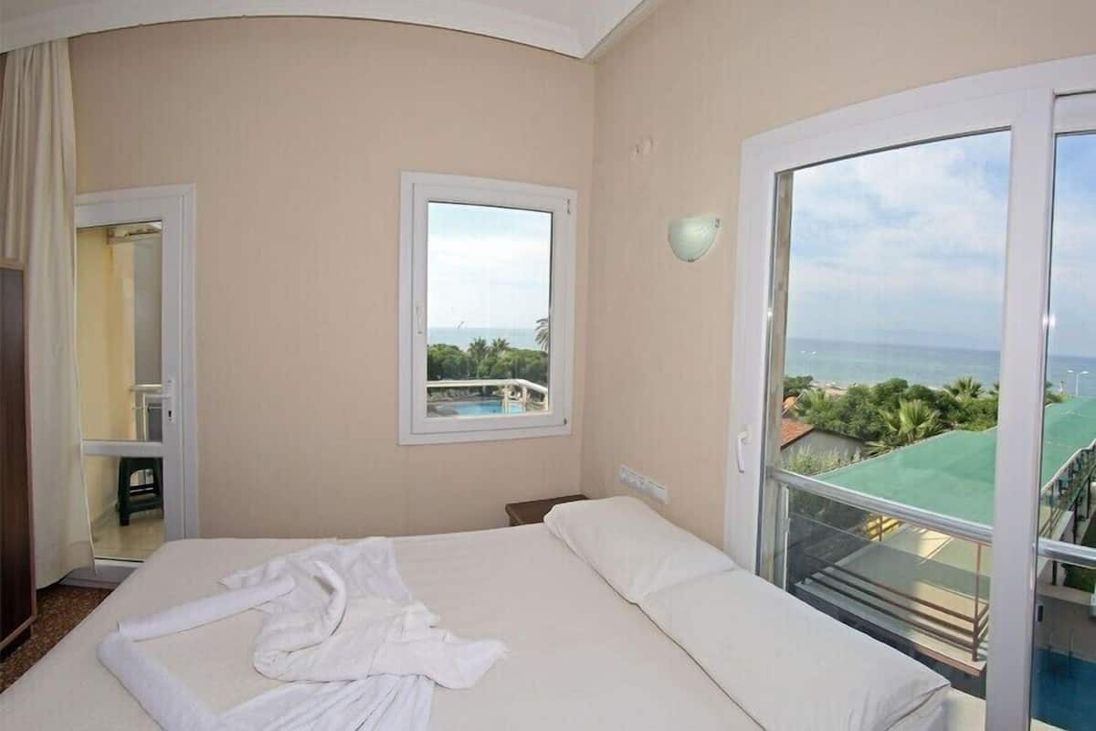 A hotel room with a bed, a window with a view of a pool and greenery, and a balcony with a railing.