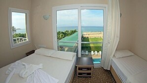 A hotel room with two beds, a balcony with a view of the beach, and a small table. - Adahan Hotel (Menderes)