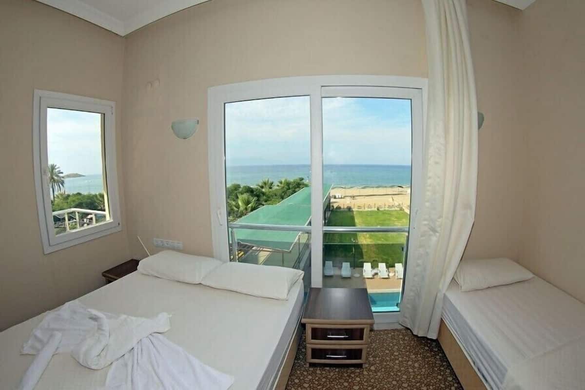 A hotel room with two beds, a balcony with a view of the beach, and a small table.