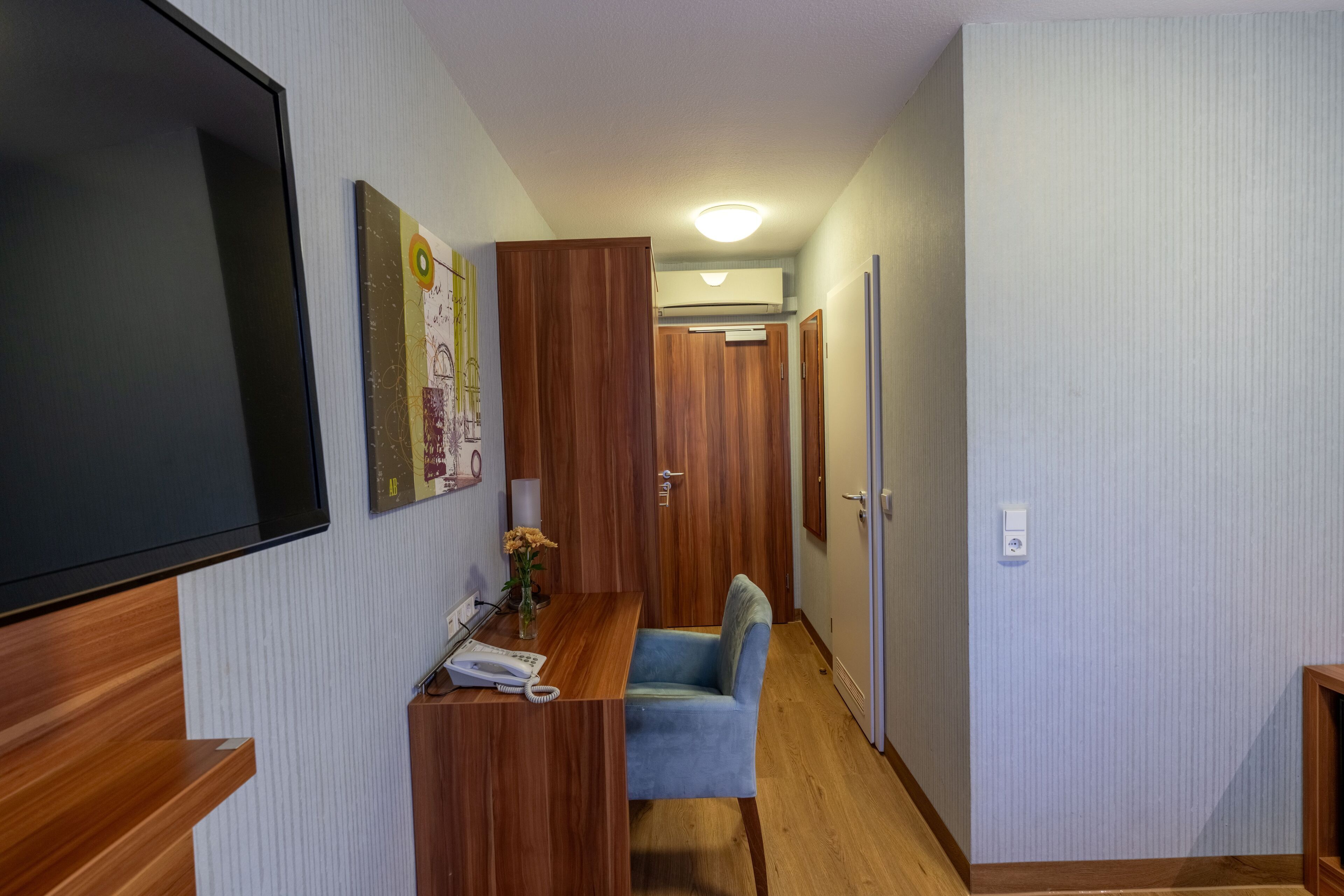 A narrow hallway with a wooden desk, a blue chair, and a television on the left.