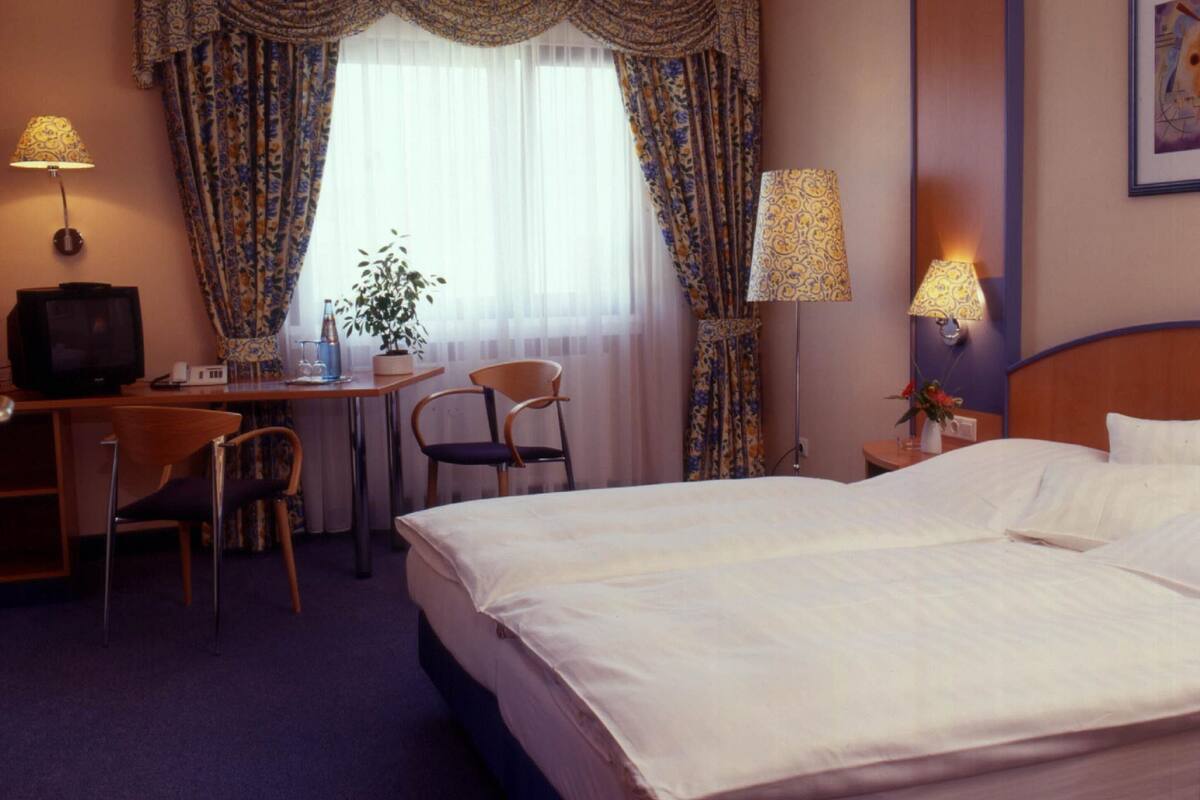 Una habitación de hotel con cama, escritorio, sillas, lámparas y televisor.