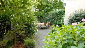 Un patio jardín con mesa y sillas, rodeado de abundante vegetación y plantas.