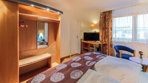 Habitación de hotel con cama, escritorio con televisor, silla y una pequeña mesa con un florero.