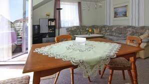 Uma área de refeições com uma mesa posta para quatro pessoas, um sofá e uma televisão ao fundo.
