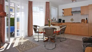 Uma sala de jantar com mesa e cadeiras, uma cozinha com armários de madeira e uma porta de vidro deslizante que dá para uma área externa.