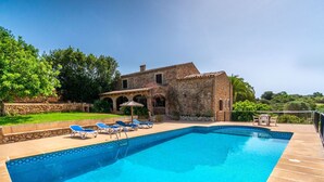 A swimming pool with lounge chairs, a stone building, and a garden.