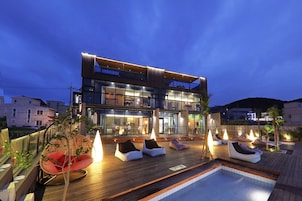 Un hotel moderno con piscina en la azotea, sillas de descanso y un espacio exterior bien iluminado.