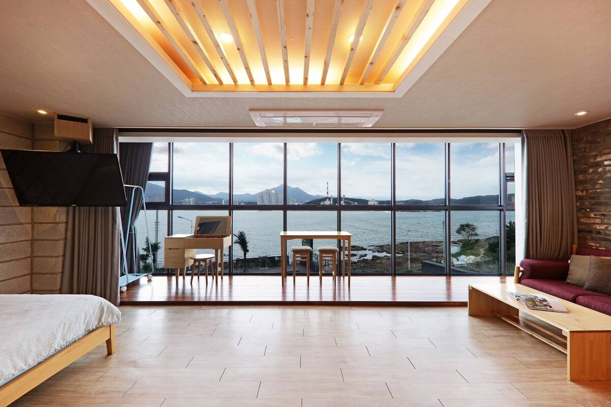 A modern hotel room with a large window offering a view of a body of water and distant mountains.