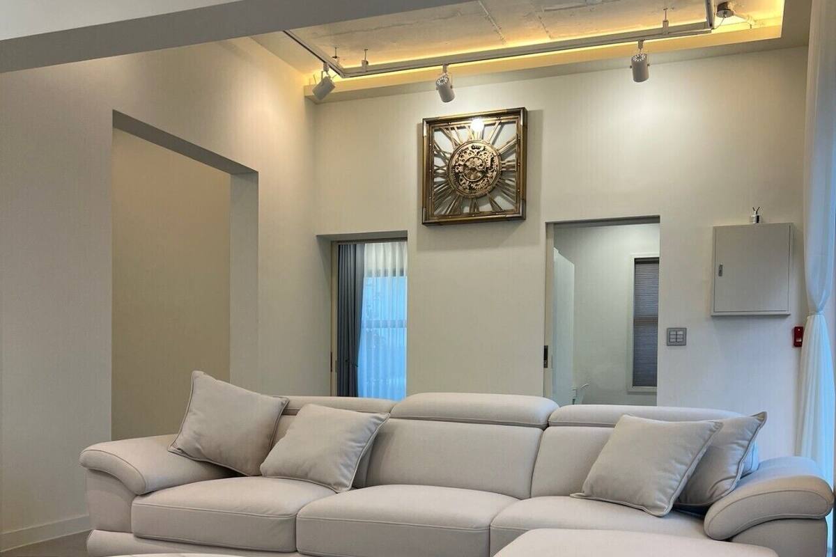 A modern living room with a beige sectional sofa, a round coffee table, and a large wall clock.