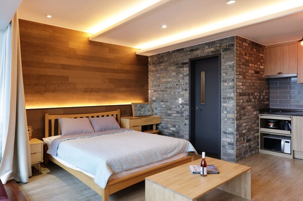 A modern bedroom with a wooden bed, bedside tables, a built-in TV, and a kitchen area with a microwave.