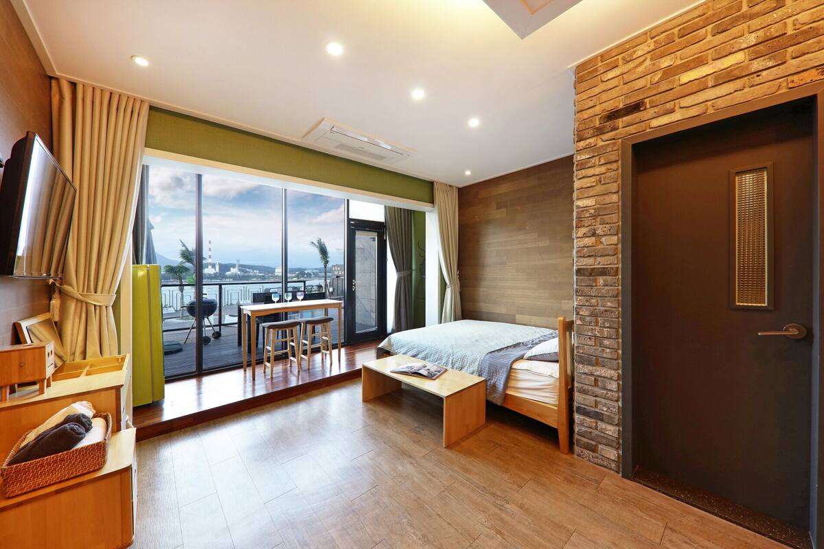 A modern hotel room with a balcony, a bed, a desk, and a TV.