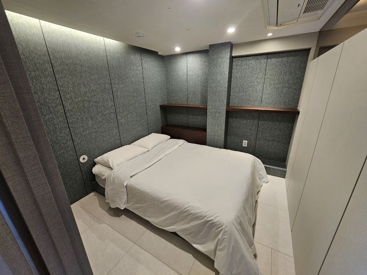 A modern bedroom with a bed, built-in shelving, and a grey textured wall.