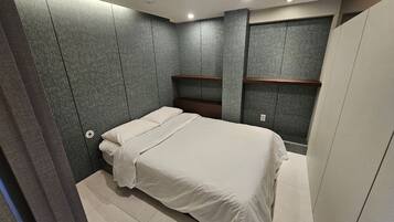 A modern bedroom with a bed, built-in shelving, and a grey textured wall.