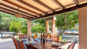 Un'area pranzo all'aperto con un tavolo in legno apparecchiato per sei persone, circondato da sedie.
