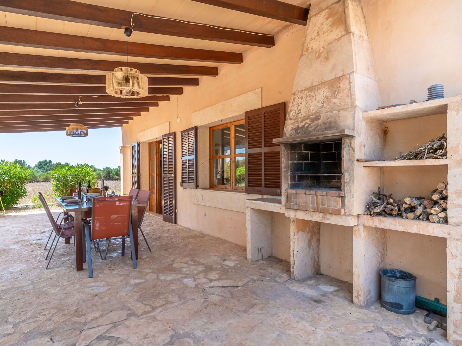 An outdoor patio with stone flooring, a table with chairs, a hanging light fixture, and a brick oven.