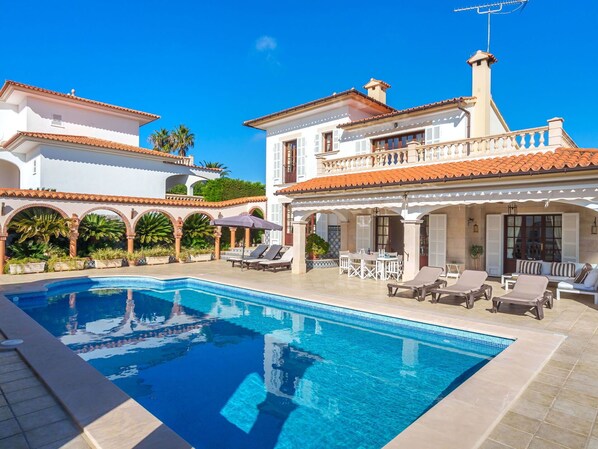 A swimming pool with lounge chairs and umbrellas, surrounded by a white building with a tiled roof and arches. - Beautiful private villa for 6 people with private pool, A/C, WIFI, TV, terrace and panoramic view (Manacor)