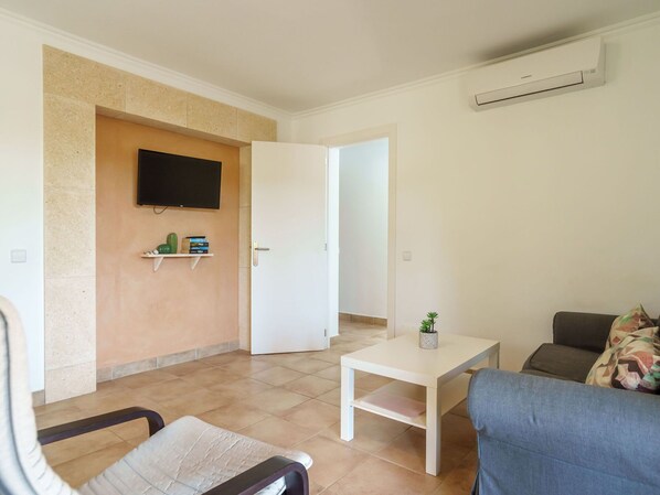 A living room with a TV mounted on the wall, a small table with a plant, a sofa, and a chair. - Beautiful apartment for 4 guests with A/C, WIFI, TV and terrace (Manacor)